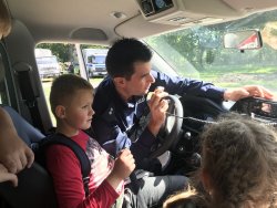 umundurowany policjant pokazuje chłopcu radiostację, chłopiec siedzi na miejscu kierowcy radiowozu.