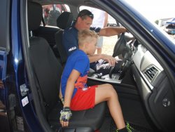 Policjanci drogówki prezentują radiowóz na zlocie miłośników BMW. Zdjęcie wnętrza radiowozu. W środku siedzi policjant i chłopiec.