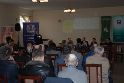 Umundurowany policjant omawia aplikację &amp;quot;Moja Komenda&amp;quot; oraz &amp;quot;Krajową Mapę Zagrożeń Bezpieczeństwa&amp;quot;. Na zdjęciu widoczni są też uczestnicy debaty.